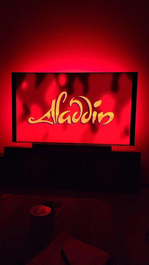 The Aladdin movie title glows on a TV screen, illuminated by vibrant red Philips Hue lights.
