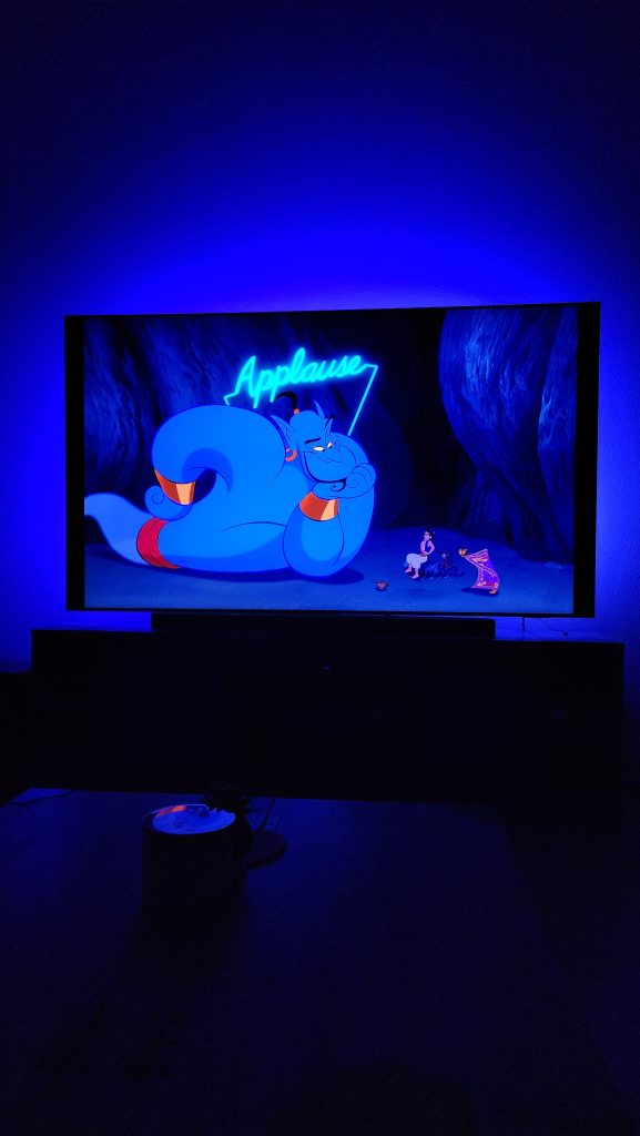 Genie appears on the TV screen with neon blue Philips Hue lights creating an electrifying glow around him.
