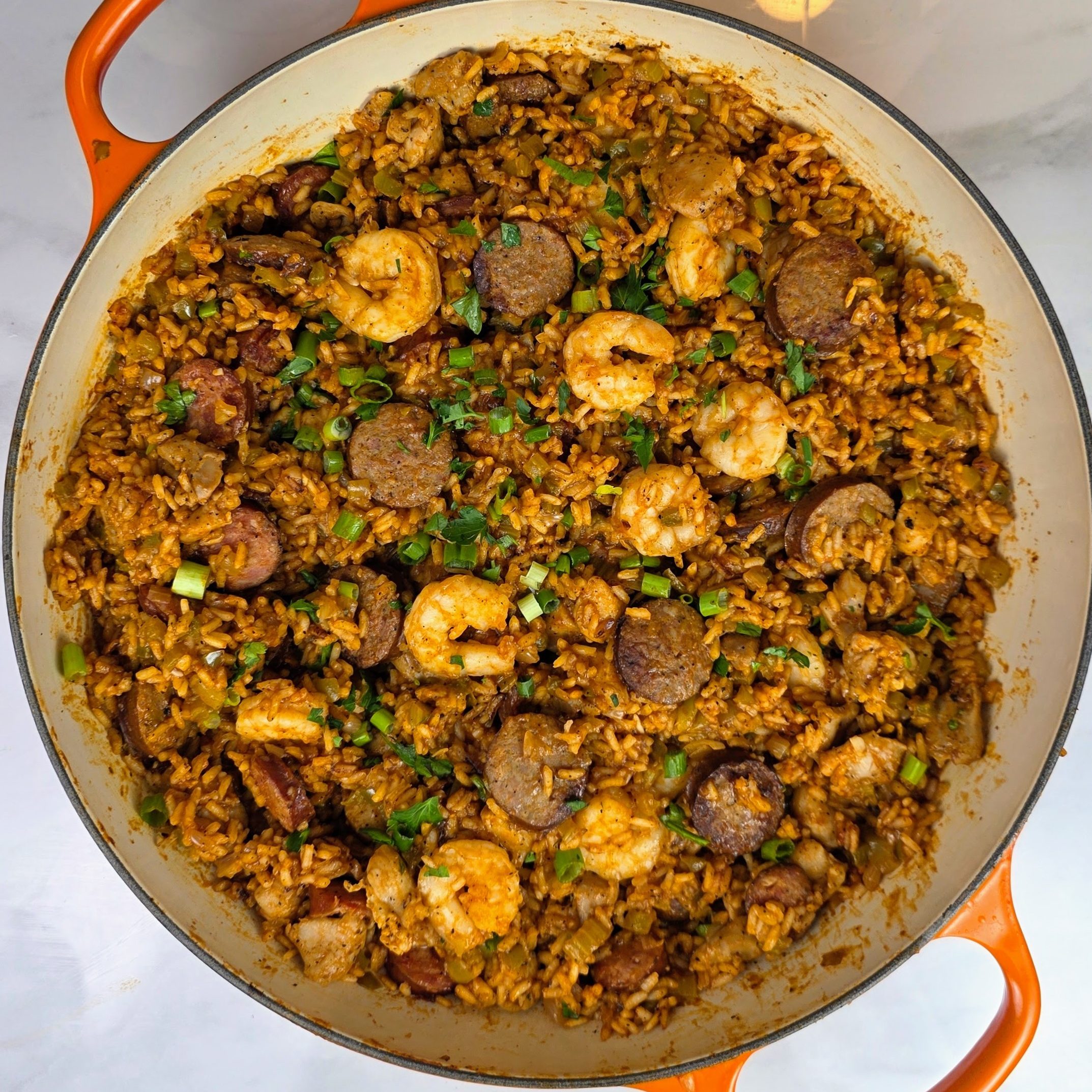 A large pot of homemade New Orleans-style jambalaya filled with shrimp, sausage, and seasoned rice, garnished with green onions.