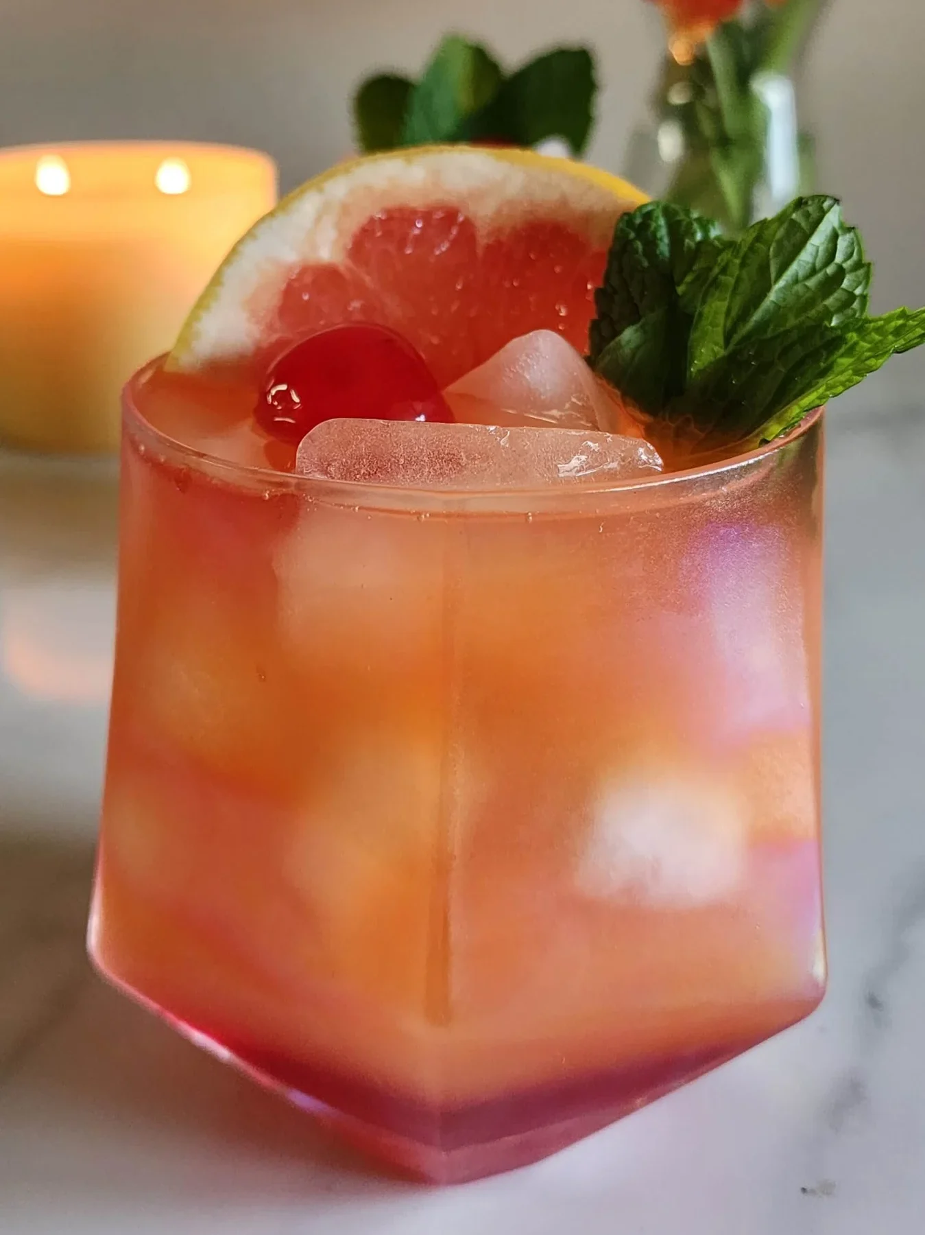 A vibrant Serengeti Sunset Cocktail, featuring citrus flavors, garnished with fresh mint, cherry, and a grapefruit slice.