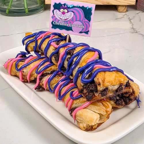 Copycat Disneyland Cheshire Cat Tails puff pastries with pink and purple icing drizzle on a white tray
